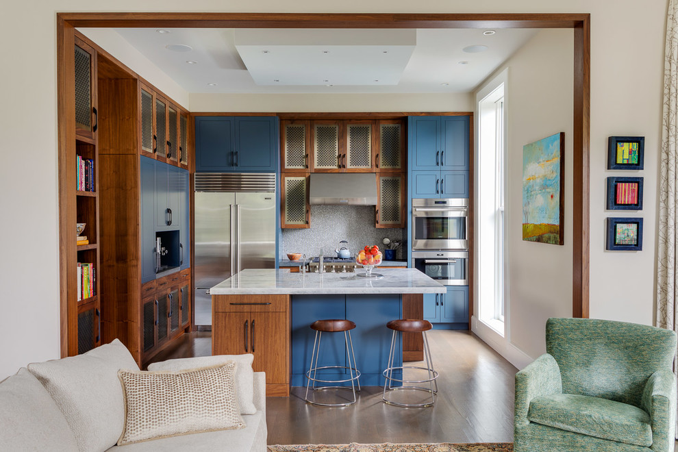 Foto på ett funkis vit l-kök, med luckor med infälld panel, blå skåp, grått stänkskydd, rostfria vitvaror, mörkt trägolv, en köksö och brunt golv