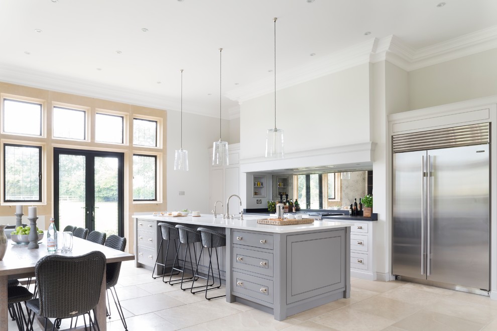 Large traditional galley open plan kitchen in Essex with an island, a double-bowl sink, metallic splashback, mirror splashback, stainless steel appliances and limestone flooring.