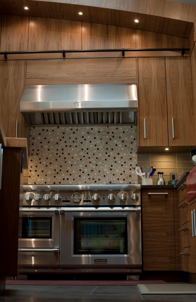 Пример оригинального дизайна: большая угловая кухня в современном стиле с обеденным столом, с полувстраиваемой мойкой (с передним бортиком), плоскими фасадами, фасадами цвета дерева среднего тона, стеклянной столешницей, серым фартуком, фартуком из плитки мозаики, техникой из нержавеющей стали, полом из керамической плитки и островом