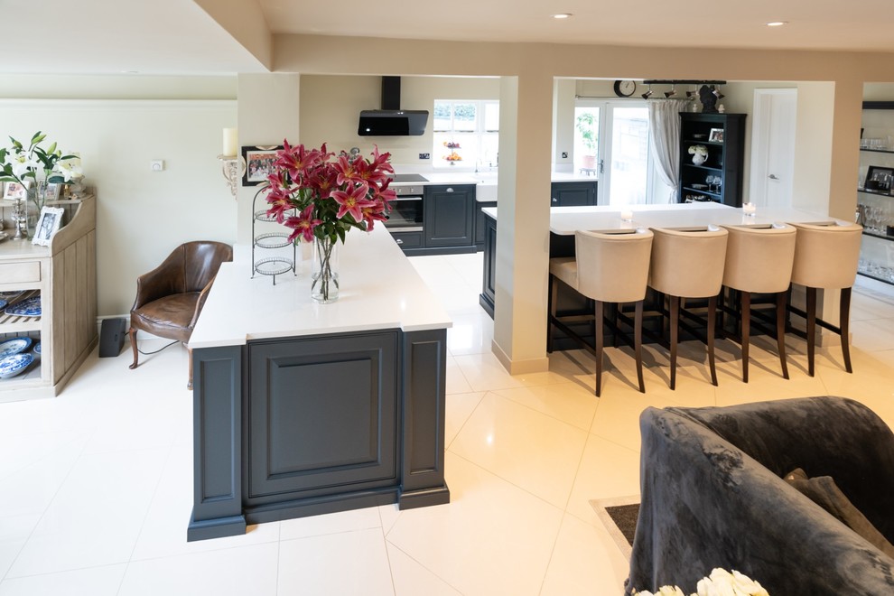 Large victorian l-shaped open plan kitchen in Essex with a double-bowl sink, raised-panel cabinets, blue cabinets, quartz worktops, ceramic flooring, an island, beige floors and white worktops.