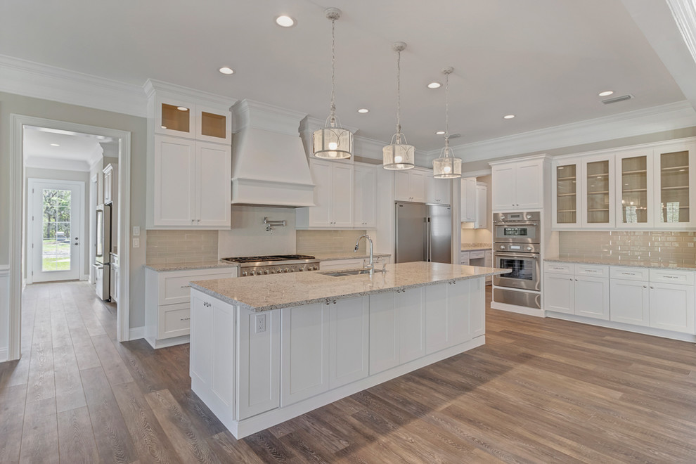 Example of a large cottage single-wall vinyl floor and brown floor eat-in kitchen design in Jacksonville with a double-bowl sink, shaker cabinets, white cabinets, granite countertops, beige backsplash, glass tile backsplash, stainless steel appliances, an island and beige countertops
