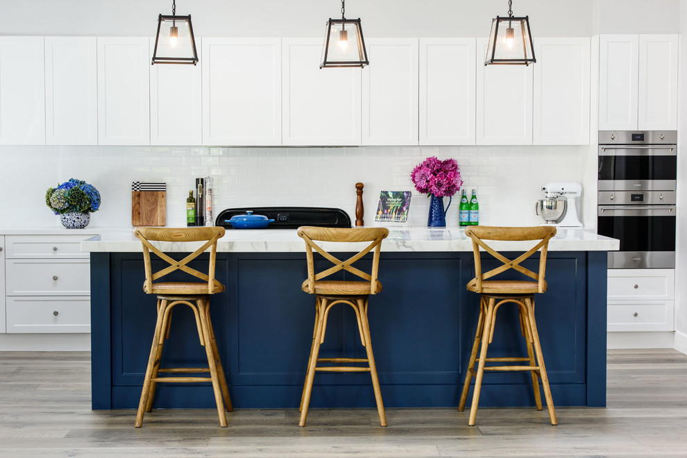 メルボルンにあるトランジショナルスタイルのおしゃれなキッチン (シェーカースタイル扉のキャビネット、白いキャビネット、白いキッチンパネル、サブウェイタイルのキッチンパネル、シルバーの調理設備、淡色無垢フローリング、ベージュの床) の写真