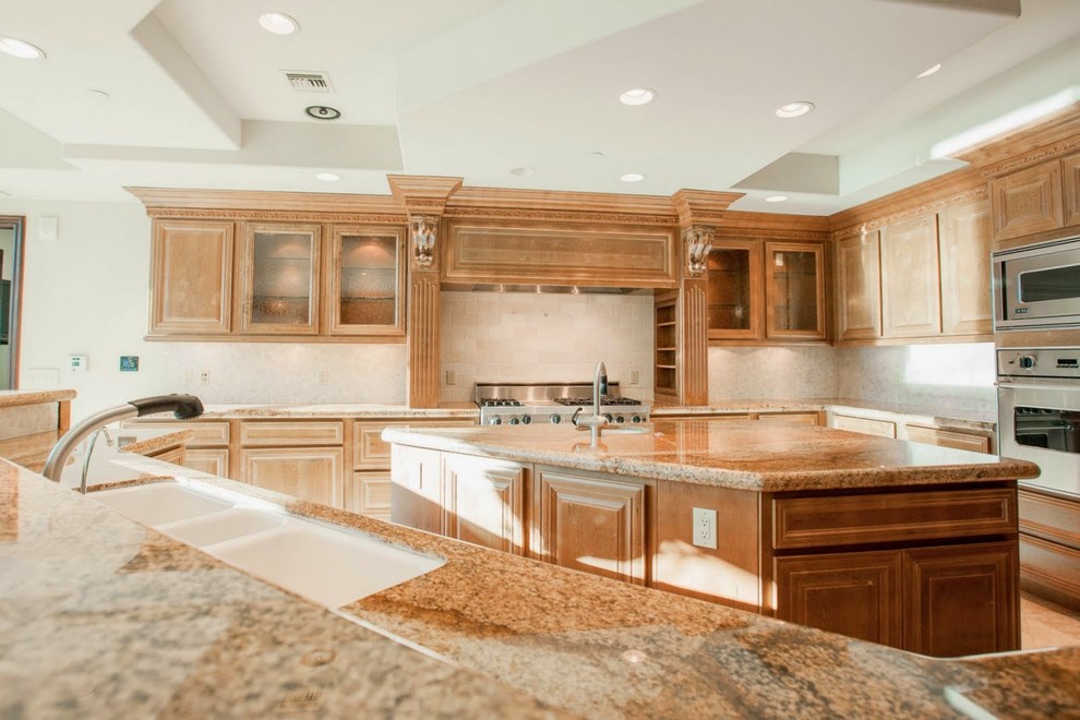 Cette image montre une grande cuisine ouverte en U et bois brun avec un évier 3 bacs, un électroménager en acier inoxydable, un sol en marbre et îlot.
