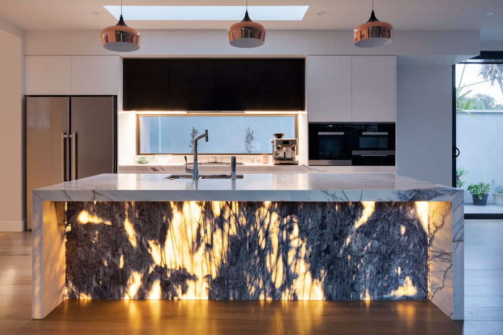 Immagine di una grande cucina minimalista con lavello sottopiano, ante nere, top in marmo, elettrodomestici in acciaio inossidabile, parquet chiaro, pavimento beige e top bianco