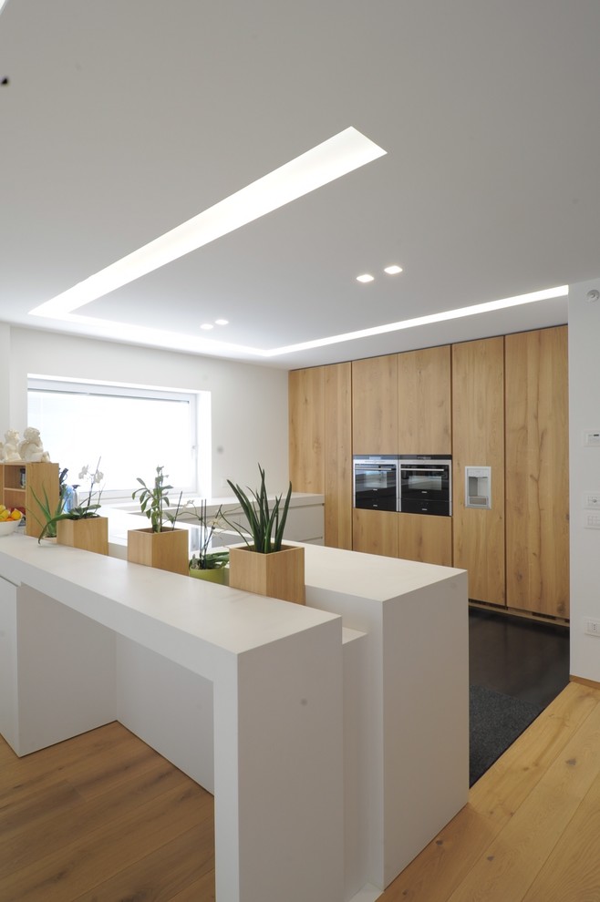 Große Moderne Küche in U-Form mit flächenbündigen Schrankfronten, hellbraunen Holzschränken, braunem Holzboden, Halbinsel und schwarzen Elektrogeräten in Sonstige