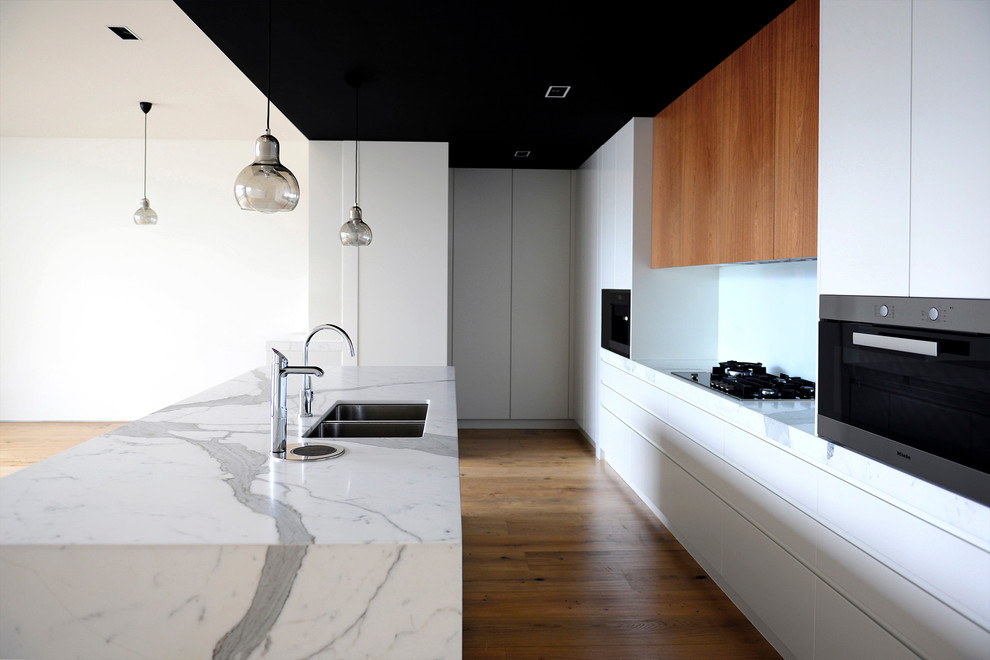 Immagine di una cucina minimal di medie dimensioni con lavello sottopiano, ante bianche, top in marmo, paraspruzzi bianco, paraspruzzi in marmo, elettrodomestici in acciaio inossidabile, pavimento in laminato e pavimento beige