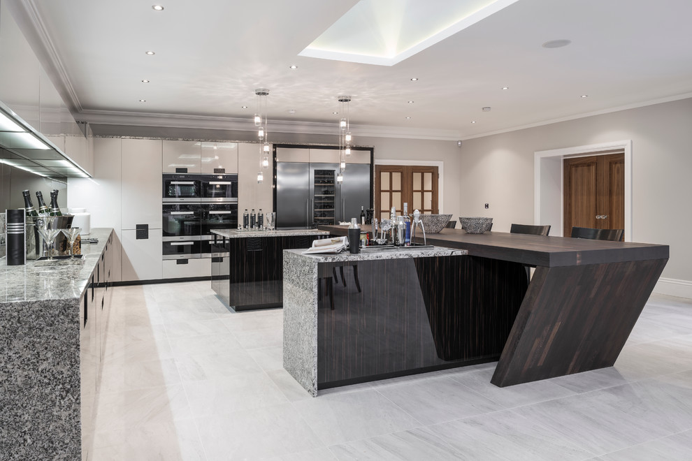 Expansive contemporary l-shaped open plan kitchen in Buckinghamshire with flat-panel cabinets, stainless steel appliances, dark wood cabinets, granite worktops, multi-coloured splashback, stone slab splashback and multiple islands.