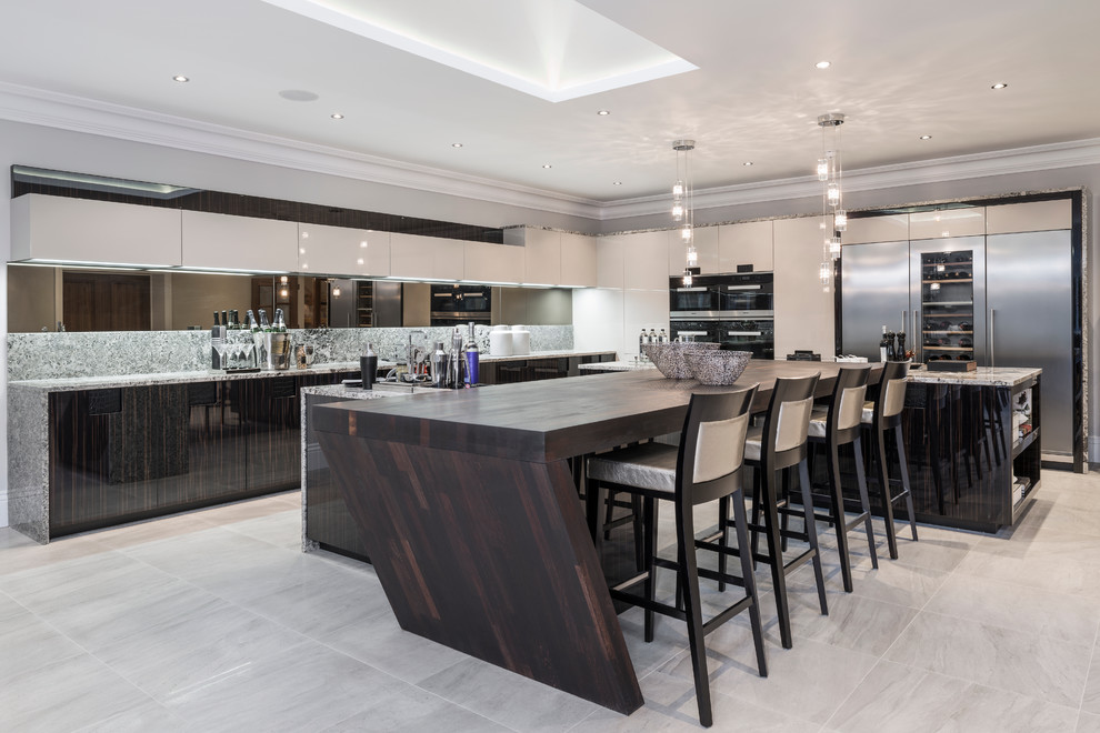 This is an example of an expansive contemporary l-shaped open plan kitchen in Buckinghamshire with flat-panel cabinets, dark wood cabinets, granite worktops, multi-coloured splashback, stone slab splashback, stainless steel appliances and multiple islands.
