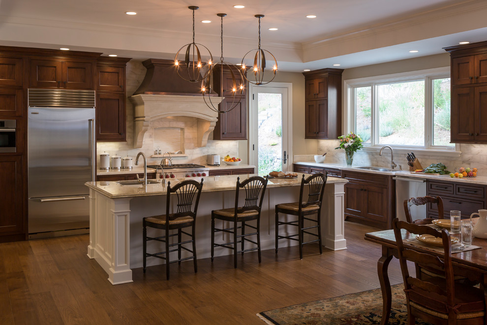 Example of a large classic l-shaped medium tone wood floor open concept kitchen design in San Francisco with an undermount sink, quartzite countertops, white backsplash, stone tile backsplash, stainless steel appliances, an island, shaker cabinets and dark wood cabinets