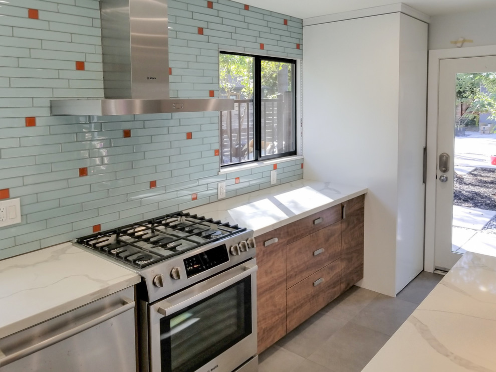 This is an example of a small nautical galley kitchen/diner in Sacramento with blue splashback, an island, white worktops, flat-panel cabinets, medium wood cabinets, engineered stone countertops, glass tiled splashback, stainless steel appliances, cement flooring and grey floors.