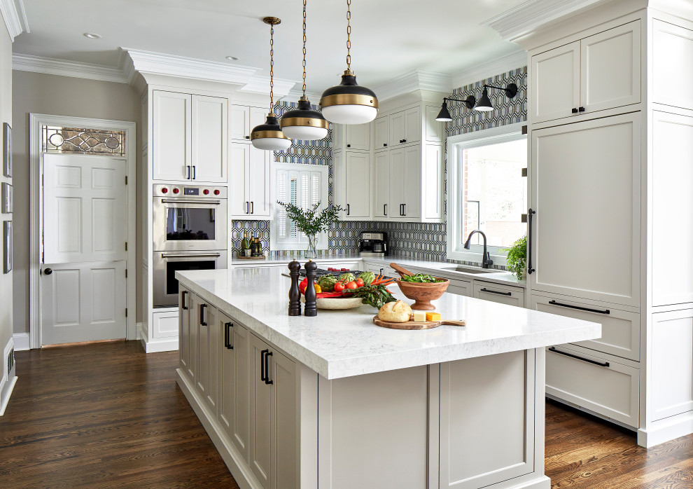 Example of a transitional l-shaped medium tone wood floor and brown floor kitchen design in Atlanta with an undermount sink, recessed-panel cabinets, white cabinets, multicolored backsplash, paneled appliances, an island and white countertops