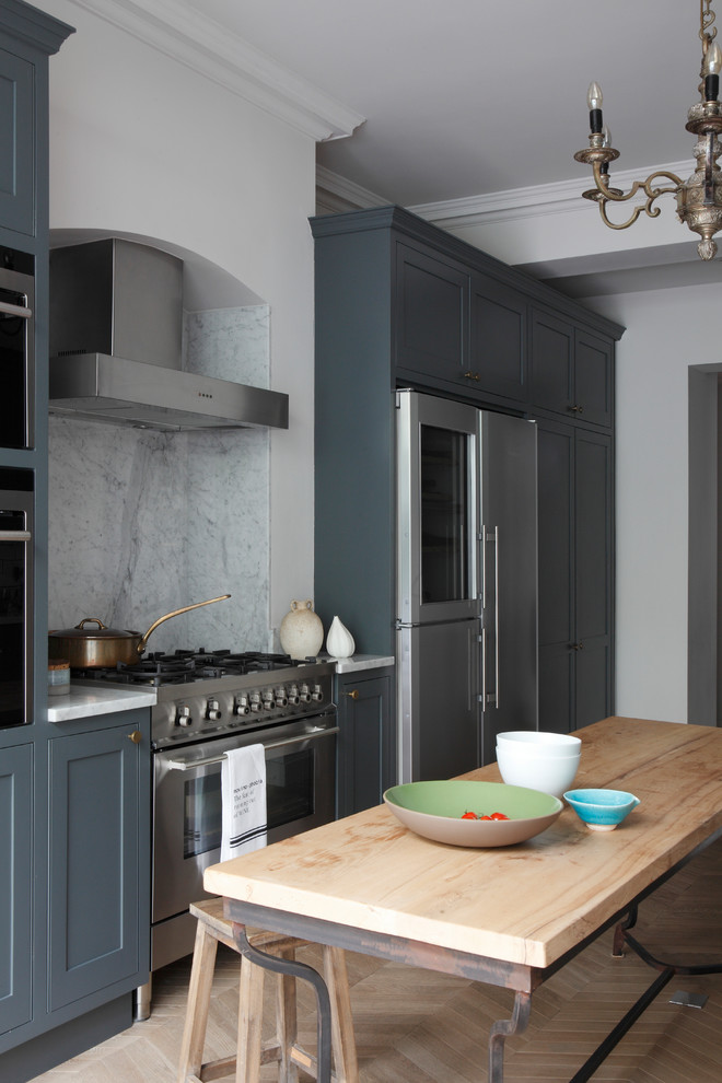 Inspiration for a large traditional galley open plan kitchen in London with a belfast sink, shaker cabinets, grey cabinets, quartz worktops, white splashback, ceramic splashback, stainless steel appliances, light hardwood flooring, a breakfast bar, brown floors and white worktops.