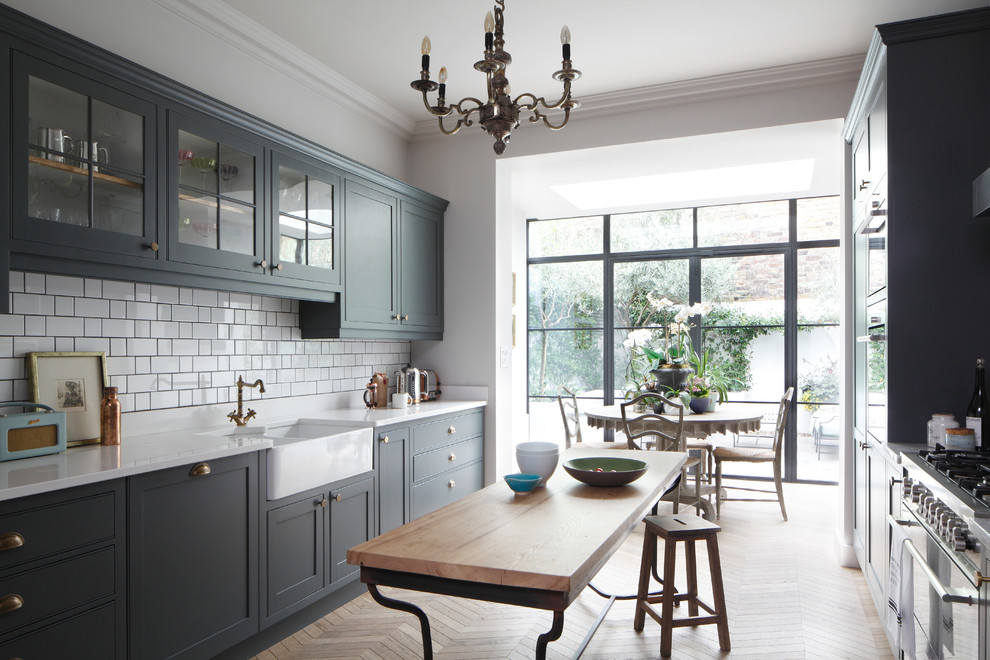 Open concept kitchen - large traditional galley light wood floor and brown floor open concept kitchen idea in London with a farmhouse sink, shaker cabinets, gray cabinets, quartzite countertops, white backsplash, ceramic backsplash, stainless steel appliances, a peninsula and white countertops