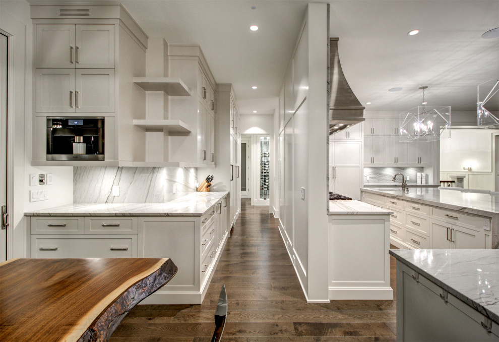 Idéer för mycket stora funkis linjära vitt kök med öppen planlösning, med en undermonterad diskho, skåp i shakerstil, vita skåp, granitbänkskiva, vitt stänkskydd, stänkskydd i skiffer, rostfria vitvaror, mellanmörkt trägolv, en köksö och brunt golv