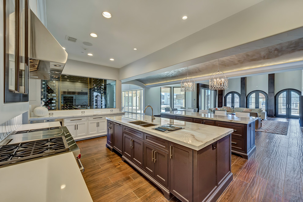 Inspiration for a huge transitional l-shaped porcelain tile and brown floor eat-in kitchen remodel in Dallas with an undermount sink, shaker cabinets, white cabinets, marble countertops, white backsplash, marble backsplash, stainless steel appliances and two islands