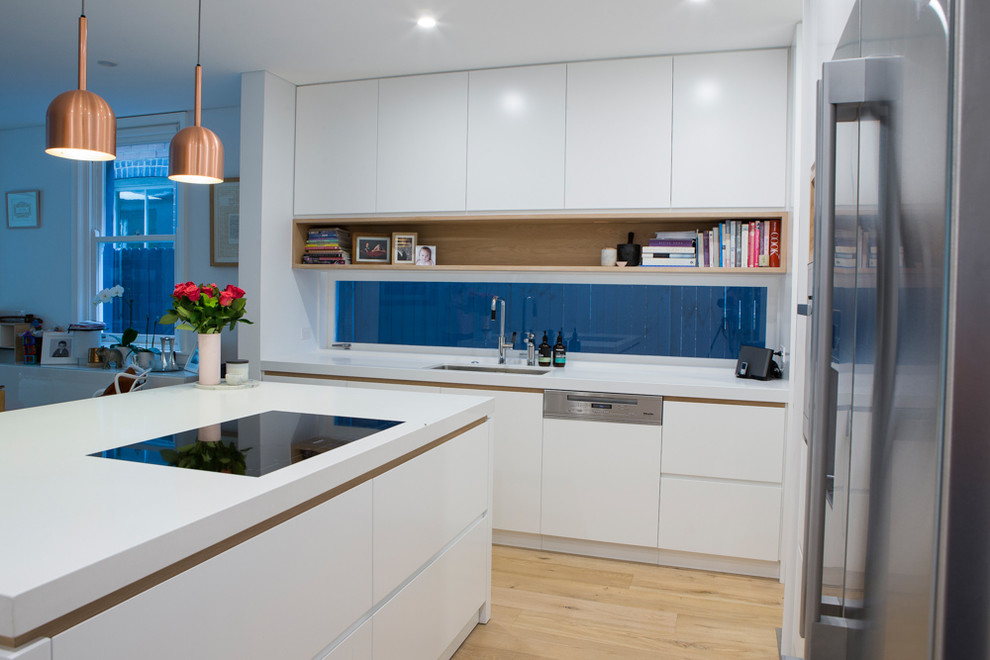 Exempel på ett stort modernt kök, med en undermonterad diskho, vita skåp, bänkskiva i kvarts, rostfria vitvaror, ljust trägolv och en köksö