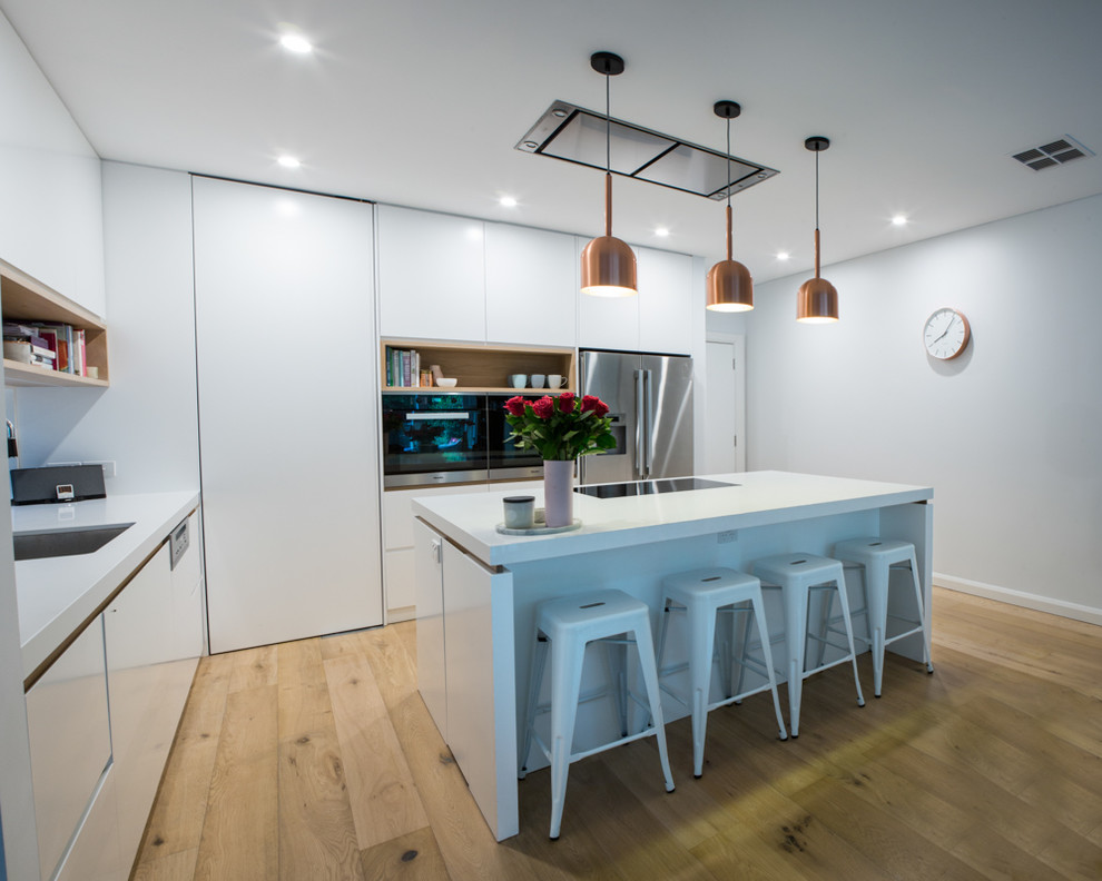 Große Moderne Wohnküche in L-Form mit Unterbauwaschbecken, weißen Schränken, Quarzwerkstein-Arbeitsplatte, Küchengeräten aus Edelstahl, hellem Holzboden und Kücheninsel in Sydney