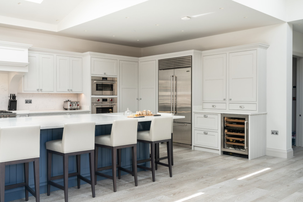 Transitional l-shaped light wood floor, beige floor, tray ceiling and vaulted ceiling kitchen photo in London with beaded inset cabinets, white cabinets, stainless steel appliances, an island and white countertops