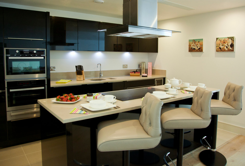 This is an example of a large modern single-wall open plan kitchen in London with a submerged sink, flat-panel cabinets, black cabinets, composite countertops, white splashback, integrated appliances, porcelain flooring and a breakfast bar.