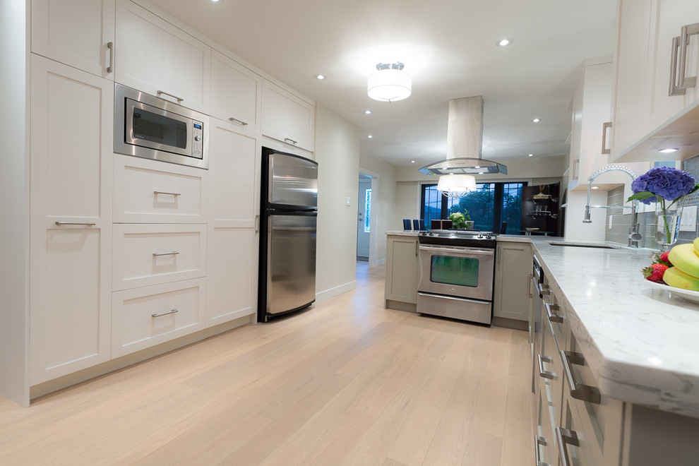 Inspiration for a large transitional l-shaped light wood floor eat-in kitchen remodel in Vancouver with an undermount sink, shaker cabinets, white cabinets, quartz countertops, green backsplash, glass tile backsplash, stainless steel appliances and a peninsula