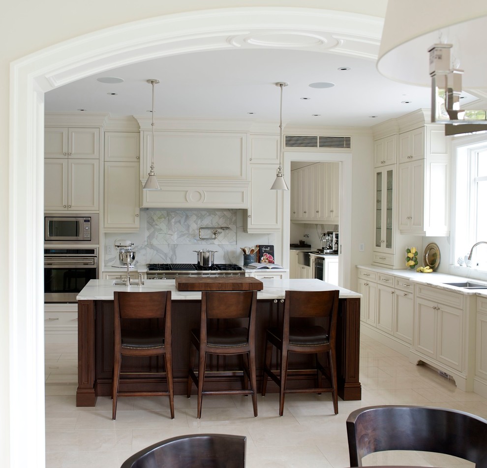 Inspiration for a large transitional u-shaped limestone floor eat-in kitchen remodel in Montreal with an undermount sink, white cabinets, marble countertops, white backsplash, stone slab backsplash, paneled appliances, an island and beaded inset cabinets