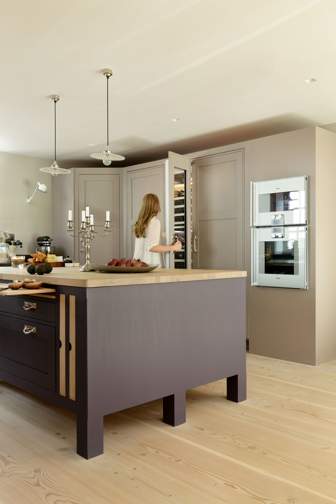 Inspiration for a large scandi u-shaped open plan kitchen in London with a double-bowl sink, shaker cabinets, composite countertops, stainless steel appliances, light hardwood flooring and an island.