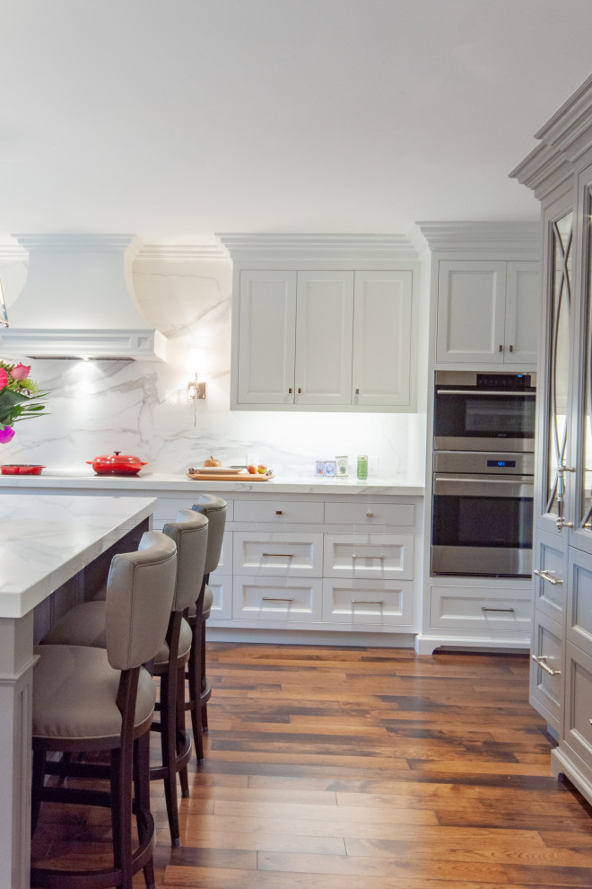 Design ideas for a large classic u-shaped kitchen pantry in Toronto with a built-in sink, beaded cabinets, white cabinets, marble worktops, white splashback, marble splashback, stainless steel appliances, dark hardwood flooring, an island, brown floors and white worktops.