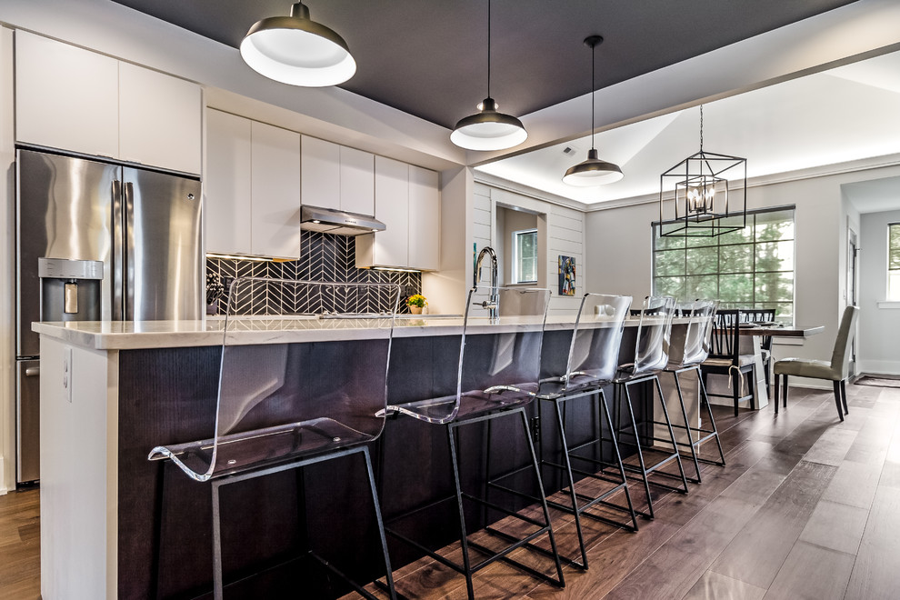 Large trendy galley dark wood floor and brown floor open concept kitchen photo in Other with an undermount sink, flat-panel cabinets, white cabinets, marble countertops, black backsplash, ceramic backsplash, stainless steel appliances and an island