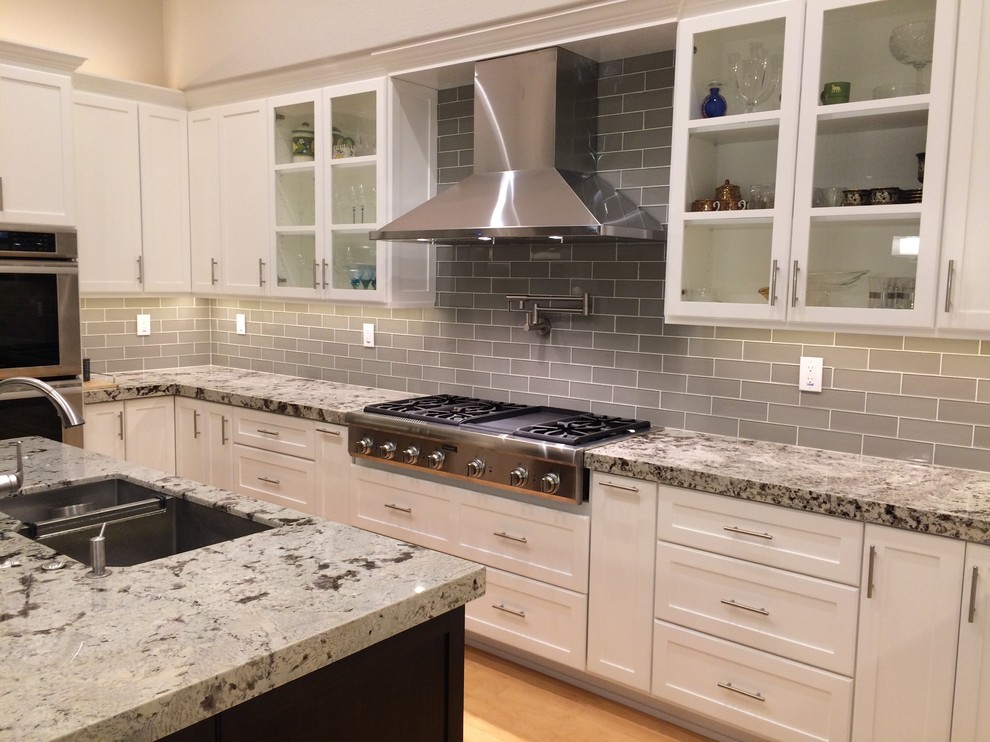 Photo of a large classic u-shaped kitchen/diner in San Francisco with a double-bowl sink, shaker cabinets, white cabinets, granite worktops, grey splashback, glass tiled splashback, stainless steel appliances, light hardwood flooring and an island.