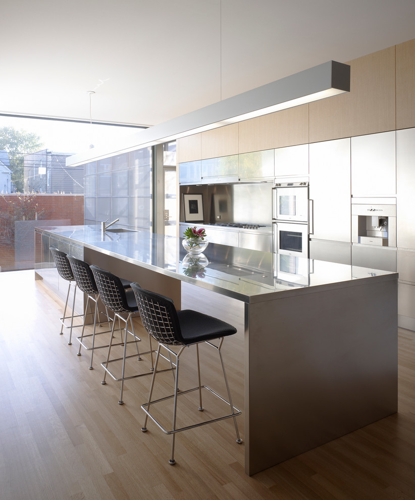 Exempel på ett litet modernt linjärt kök med öppen planlösning, med en undermonterad diskho, släta luckor, skåp i rostfritt stål, bänkskiva i rostfritt stål, stänkskydd med metallisk yta, rostfria vitvaror, ljust trägolv och en köksö