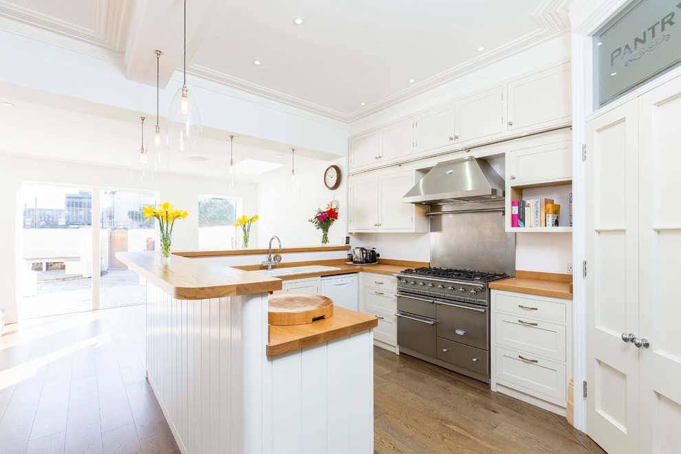 This is an example of a classic u-shaped open plan kitchen in Hampshire with shaker cabinets, white cabinets, wood worktops, stainless steel appliances and a breakfast bar.