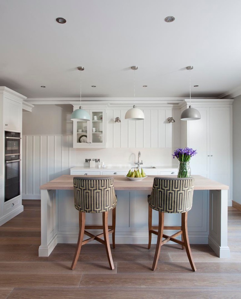 Klassische Küche in L-Form mit weißen Schränken, Arbeitsplatte aus Holz, hellem Holzboden und Kücheninsel in Dublin