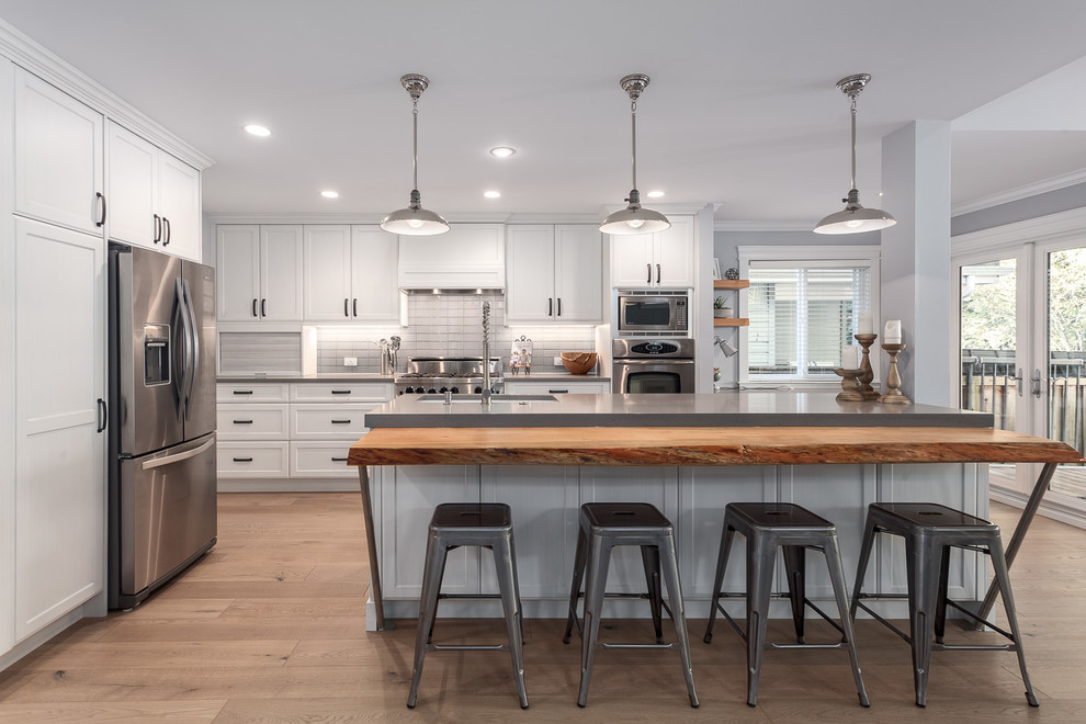 Example of a mid-sized transitional l-shaped medium tone wood floor and brown floor open concept kitchen design in Vancouver with an undermount sink, quartzite countertops, gray backsplash, subway tile backsplash, stainless steel appliances, an island, shaker cabinets and white cabinets