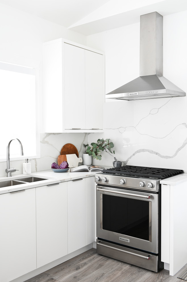 Kleine Moderne Wohnküche mit Unterbauwaschbecken, flächenbündigen Schrankfronten, weißen Schränken, Küchenrückwand in Weiß, Küchengeräten aus Edelstahl, grauem Boden, weißer Arbeitsplatte, gewölbter Decke und Laminat in Vancouver