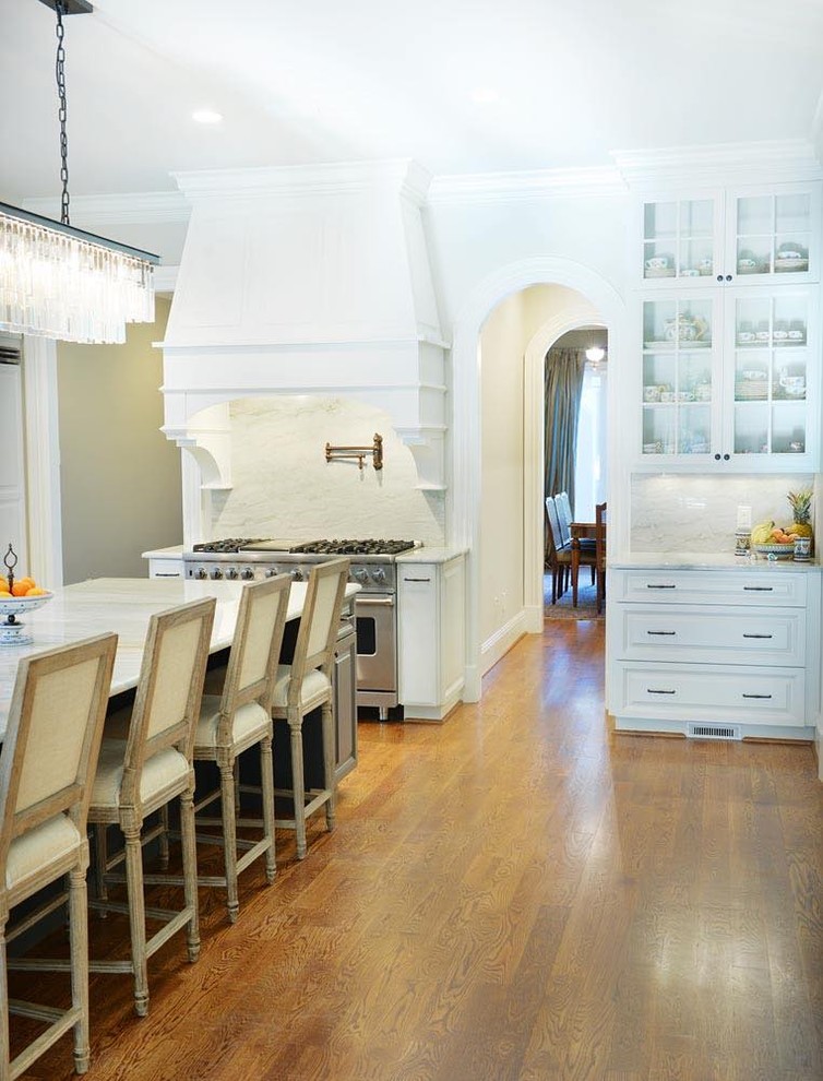 This is an example of an expansive traditional u-shaped kitchen/diner in Nashville with white cabinets, white splashback, stainless steel appliances, medium hardwood flooring and an island.