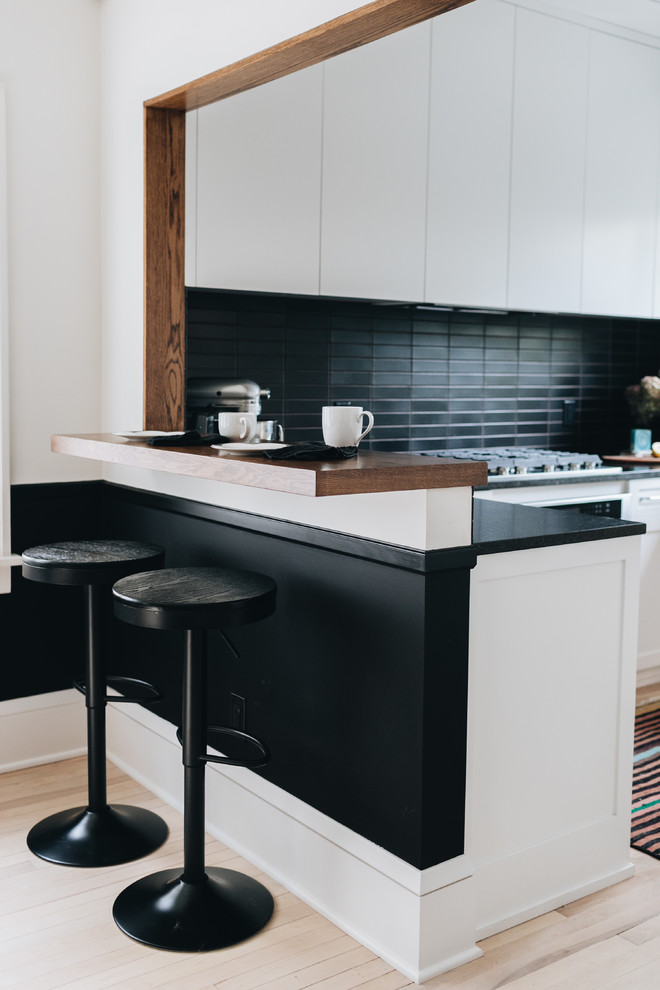 ミネアポリスにある高級な中くらいなモダンスタイルのおしゃれなキッチン (アンダーカウンターシンク、フラットパネル扉のキャビネット、白いキャビネット、御影石カウンター、黒いキッチンパネル、テラコッタタイルのキッチンパネル、パネルと同色の調理設備、淡色無垢フローリング、白い床) の写真