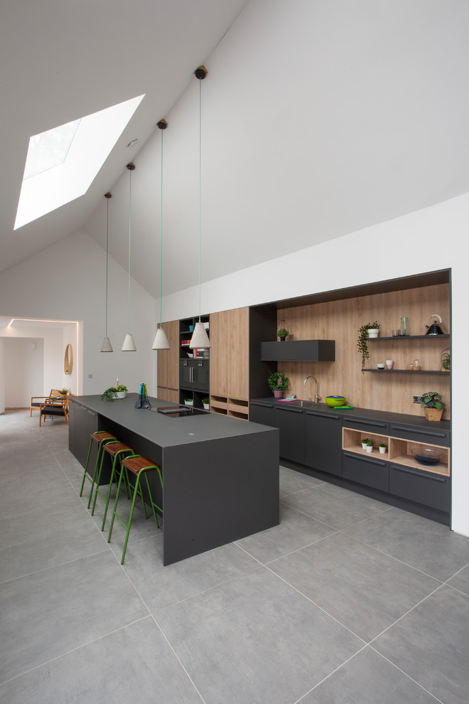 Zweizeilige Moderne Küche mit flächenbündigen Schrankfronten, schwarzen Schränken, Küchenrückwand in Beige, Rückwand aus Holz, schwarzen Elektrogeräten, Kücheninsel, grauem Boden und schwarzer Arbeitsplatte in West Midlands