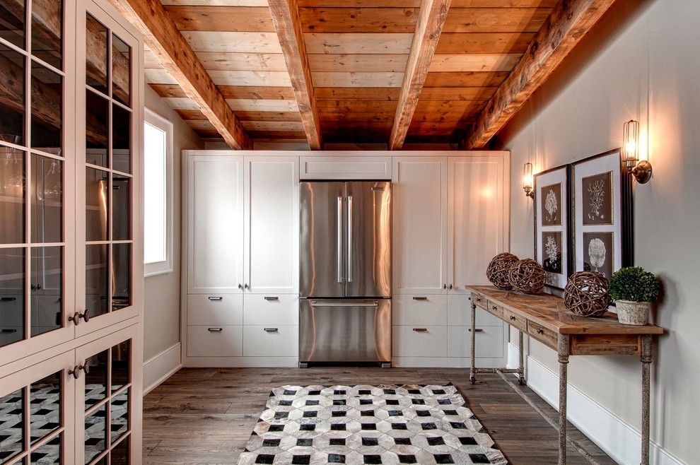 Photo of a rustic l-shaped kitchen pantry in Toronto with a belfast sink, shaker cabinets, white cabinets, engineered stone countertops, stainless steel appliances, medium hardwood flooring and an island.