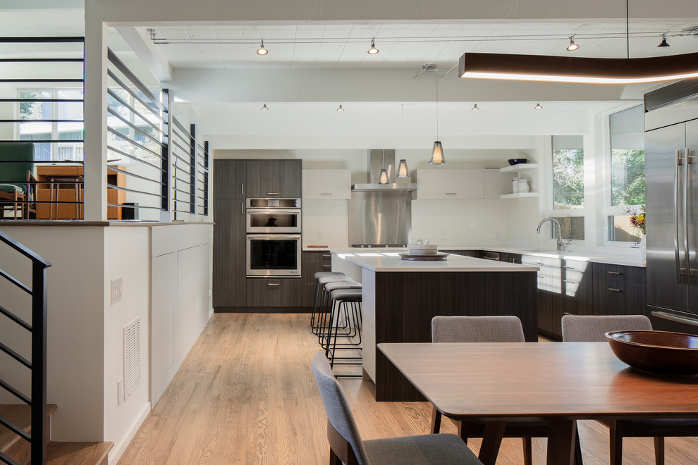 Mid-sized minimalist l-shaped medium tone wood floor and brown floor eat-in kitchen photo in Denver with an undermount sink, flat-panel cabinets, dark wood cabinets, quartz countertops, white backsplash, stainless steel appliances, an island and white countertops