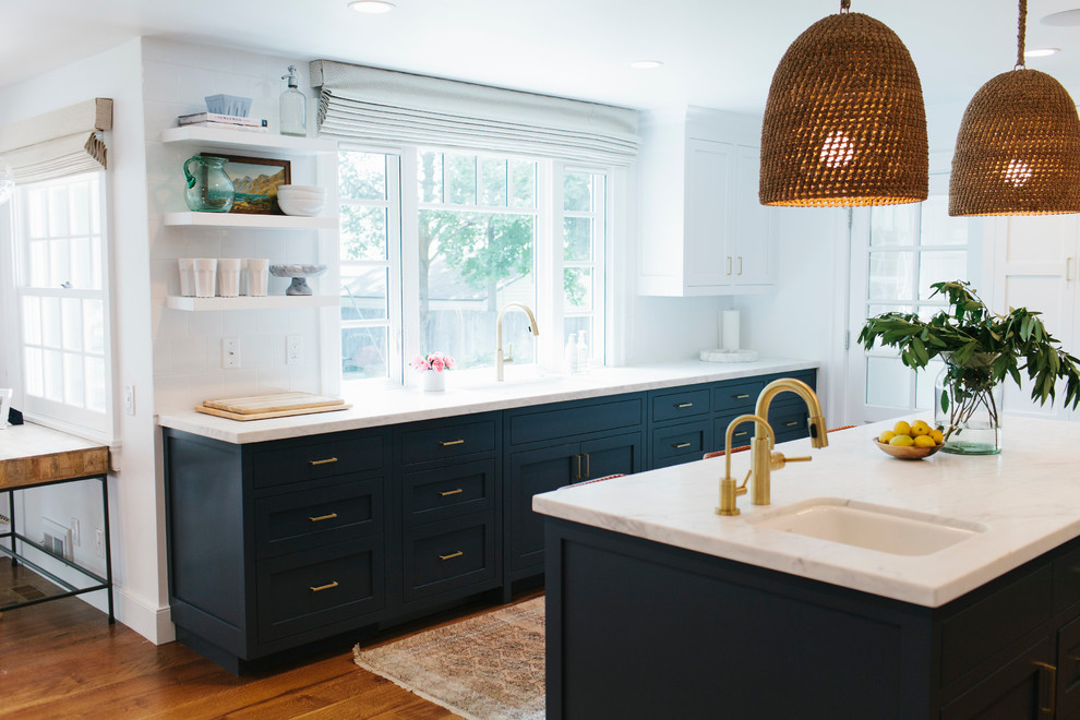 Cette photo montre une cuisine avec des portes de placard bleues, plan de travail en marbre, une crédence blanche, parquet foncé et îlot.