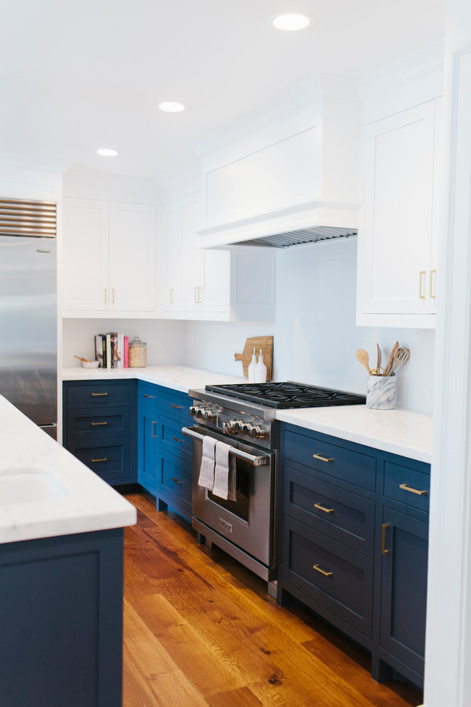 Immagine di un cucina con isola centrale con lavello da incasso, ante bianche, top in marmo, paraspruzzi bianco, elettrodomestici in acciaio inossidabile e parquet scuro