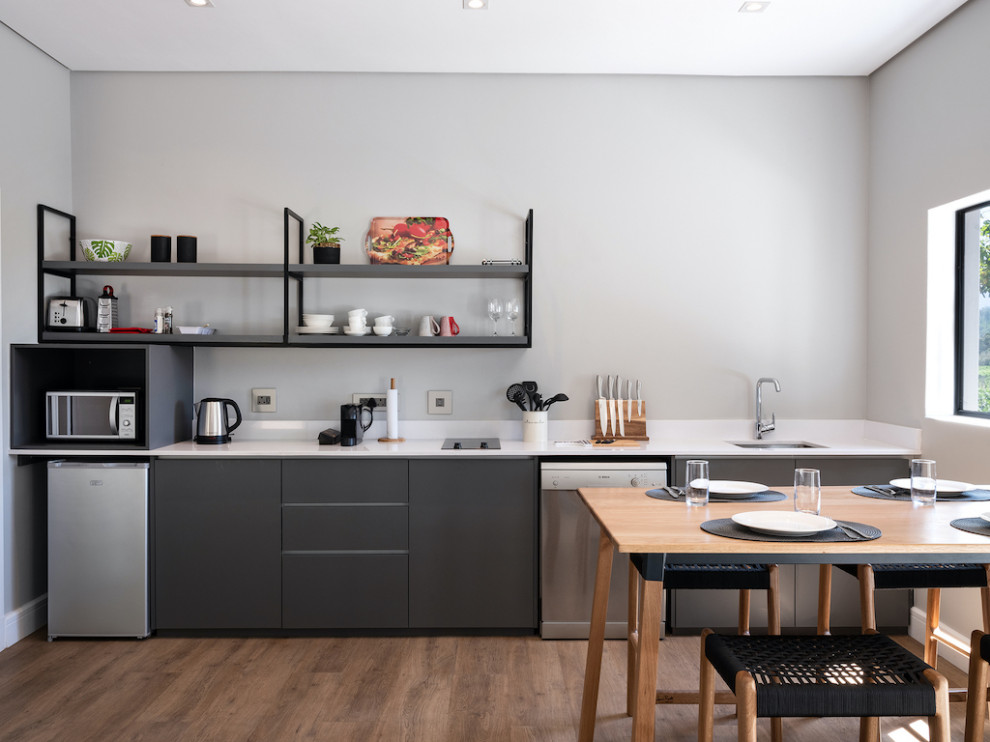Стильный дизайн: прямая кухня-гостиная среднего размера в скандинавском стиле с врезной мойкой, цветной техникой, полом из ламината, коричневым полом и белой столешницей - последний тренд