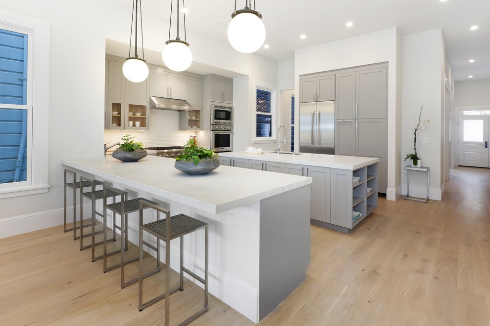 Photo of a large classic u-shaped kitchen in San Francisco with a submerged sink, shaker cabinets, grey cabinets, engineered stone countertops, white splashback, ceramic splashback, stainless steel appliances, light hardwood flooring and an island.