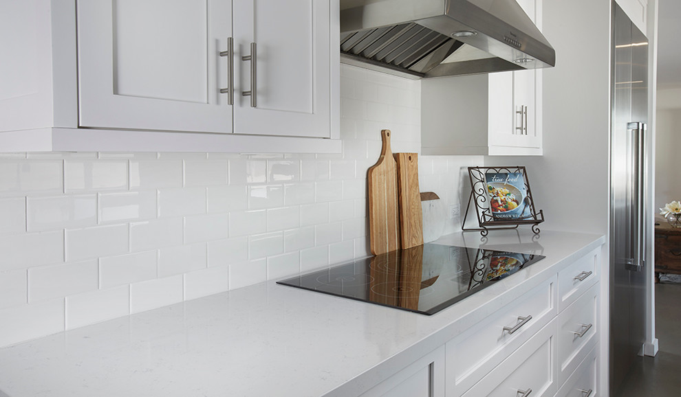 Modern inredning av ett kök, med en rustik diskho, skåp i shakerstil, bänkskiva i kvarts, vitt stänkskydd, stänkskydd i tunnelbanekakel, rostfria vitvaror, betonggolv och en köksö