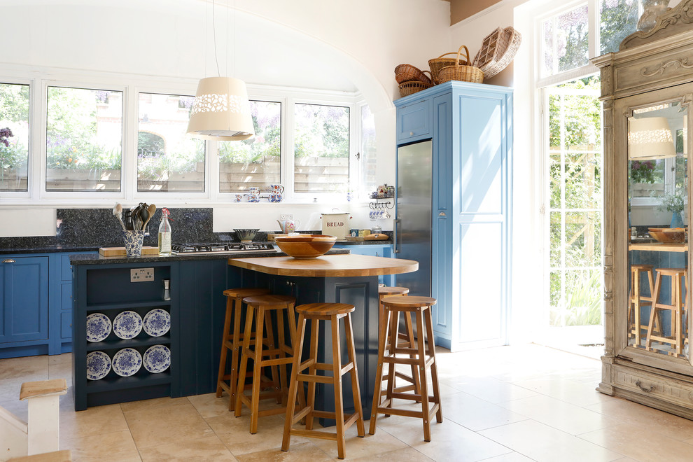 Idée de décoration pour une cuisine champêtre de taille moyenne avec des portes de placard bleues, un placard à porte shaker, une crédence noire, un électroménager en acier inoxydable, un sol beige et plan de travail noir.