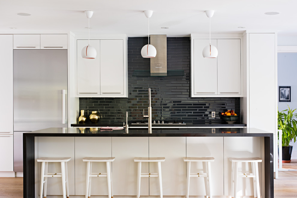 Example of a large trendy galley open concept kitchen design in Toronto with flat-panel cabinets, quartz countertops, glass tile backsplash, stainless steel appliances, an island and black backsplash