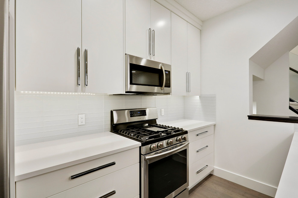 Foto på ett avskilt funkis u-kök, med en undermonterad diskho, släta luckor, vita skåp, bänkskiva i kvartsit, vitt stänkskydd, stänkskydd i glaskakel, rostfria vitvaror, ljust trägolv och en köksö