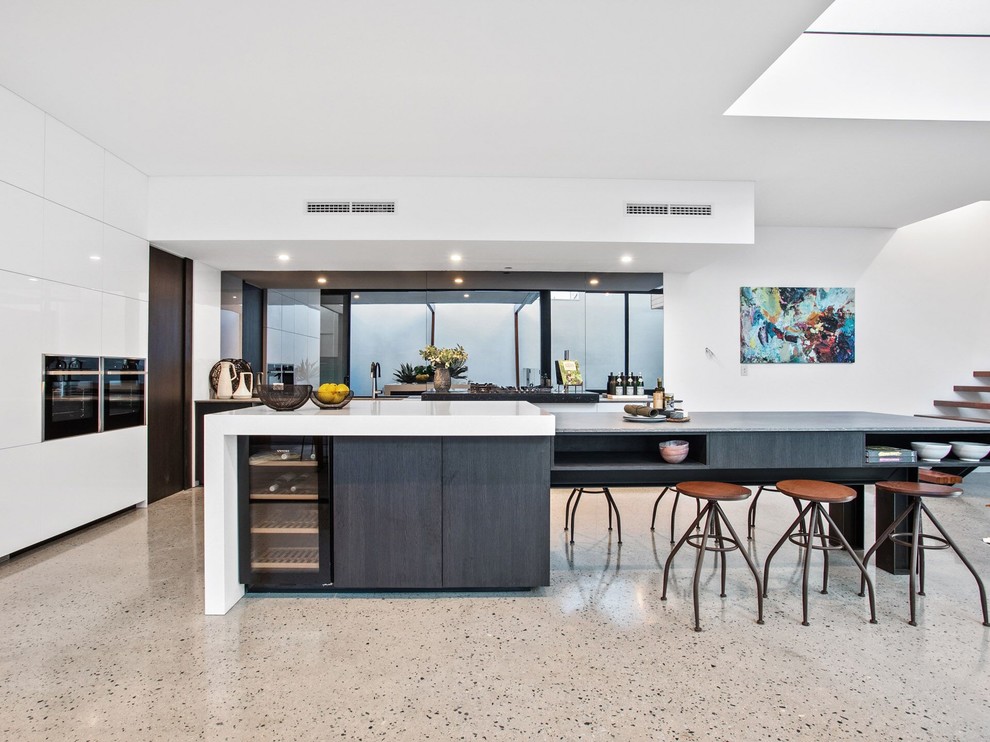 Moderne Küche in L-Form mit flächenbündigen Schrankfronten, weißen Schränken, Rückwand-Fenster, schwarzen Elektrogeräten, Betonboden, Kücheninsel, grauem Boden und weißer Arbeitsplatte in Perth