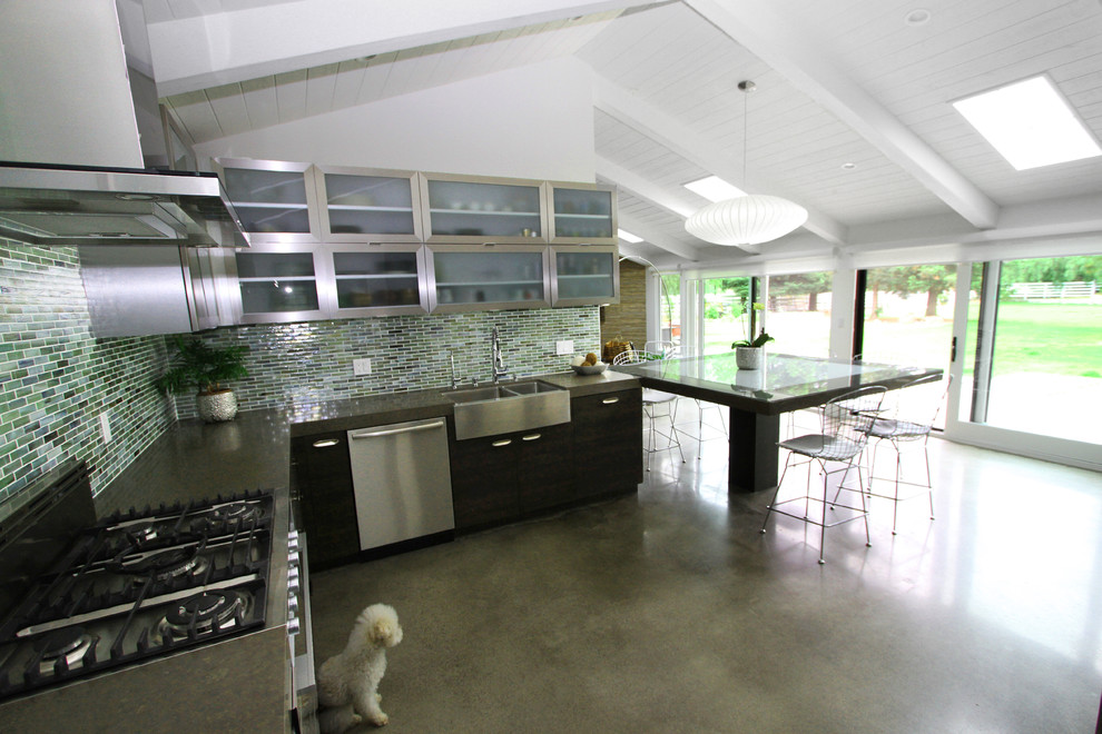 Modern inredning av ett kök, med en rustik diskho, luckor med glaspanel, skåp i rostfritt stål, bänkskiva i kvarts, blått stänkskydd, glaspanel som stänkskydd, rostfria vitvaror, betonggolv och en köksö