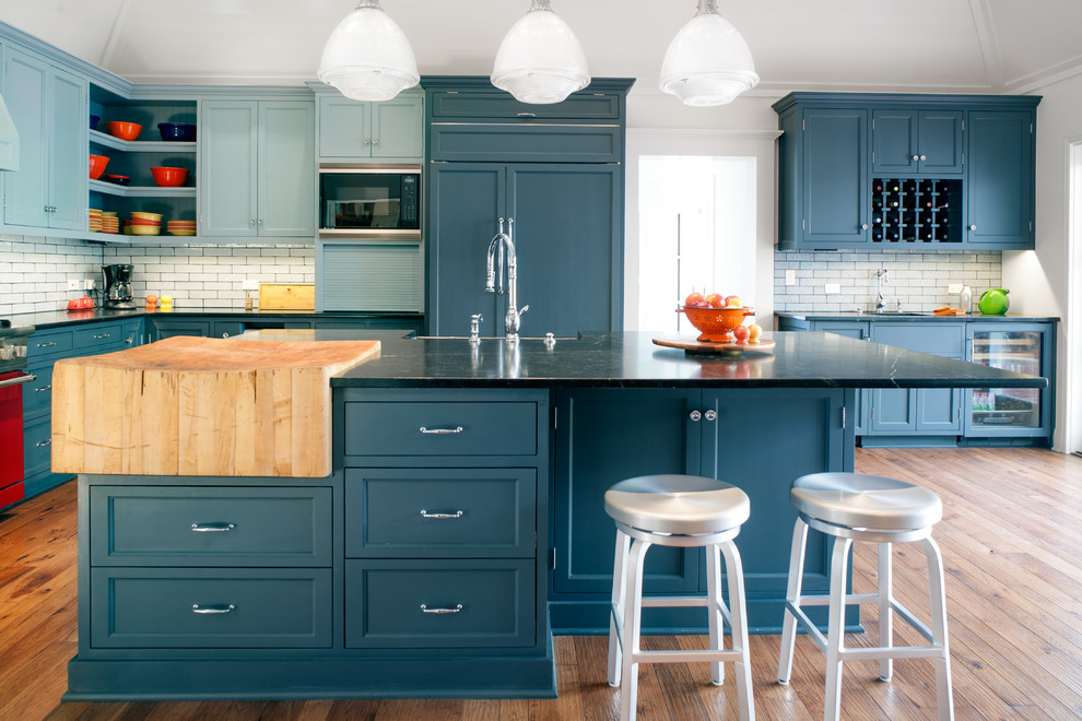 Example of a large classic l-shaped medium tone wood floor eat-in kitchen design in Los Angeles with a farmhouse sink, recessed-panel cabinets, gray cabinets, soapstone countertops, gray backsplash, paneled appliances and subway tile backsplash